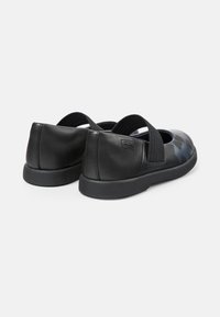 Zwarte leren schoenen met een gladde afwerking, voorzien van een blauw patroon, elastische band en platte rubberen zool. Achteraanzicht weergegeven.