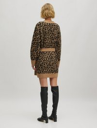 Strickkleid mit einem Leopardenmuster in Braun und Schwarz, mit einem taillierten Gürtel, langen Ärmeln und kombiniert mit kniehohen schwarzen Stiefeln.