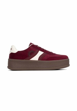 Zapatilla de plataforma baja con parte superior de ante rojo oscuro, suela gruesa marrón, cuello del talón blanco y franja lateral blanca con diseño circular.