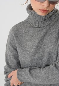 Gray knitted turtleneck sweater with a ribbed neckline and cuffs, showcasing a soft texture and relaxed fit.