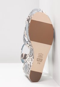 Vue de la semelle d'une sandale en cuir imprimé serpent taille 4,5, montrant les coussinets marron du talon et de la plante du pied ainsi que toutes les marques en cuir.