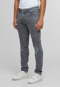 Harmaat slim-fit farkut, joissa on urheilullisia yksityiskohtia ja kulutettuja efektejä. Varustettu viidellä taskulla ja punaisella tarralla vyötäröllä. Yhdistettynä valkoisiin lenkkareihin.