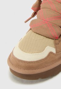 Sneaker in suede marrone con parte superiore in mesh beige, dettagli testurizzati e motivo rosa nell'area dei lacci. Punta arrotondata e suola in gomma.