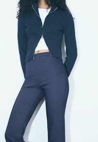 Námořnický svetr na zip s těsným střihem, žebrovanou strukturou a stříbrným zipem, doplněný o tmavě modré kalhoty s vysokým pasem z hladké tkaniny.
