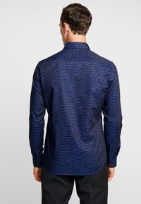 Mörkblå långärmad skjorta med subtilt vågmönster, knäppte manschetter och klassisk krage, tillverkad av mjuk tyg.