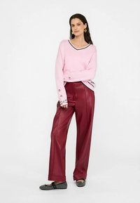 Světle růžový pletený svetr s výstřihem do V a černými detaily, doplněný vínově červenými širokými kalhotami z umělé kůže. Černé baleríny s ozdobami.