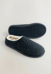 Tmavě modré látkové bačkůrky s texturovaným povrchem, bílým umělým kožíškem uvnitř a černou gumovou podrážkou se zigzagovým vzorem.