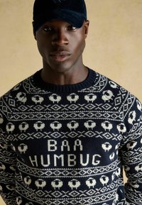 Marineblaues Strickpullover mit Schafen und Herzmustern, mit der Aufschrift "BAA HUMBUG" in Weiß. Gerippter Kragen und Bündchen, weiche Textur.