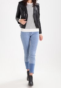 Svart läderbikerjacka över en vit mönstrad tröja, matchad med ljusblå slim-fit jeans med en färgblockering vid fållen. Svarta anklar stövlar.