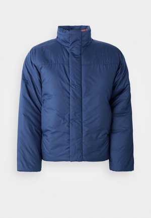 Doudoune bleu marine avec col haut, fermeture à glissière à l'avant et texture matelassée. Présente un logo sur la zone du côté gauche de la poitrine.