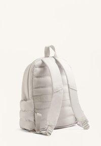 Párnázott fehér hátizsák állítható pántokkal, tetején fogantyúval és oldalsó zsebekkel, sima felülettel és strukturált kialakítással.