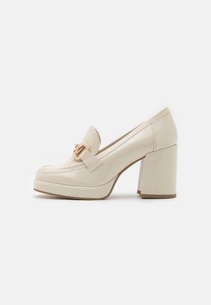 Mocassins à talons beige en cuir texturé, dotés d'une large sangle avec des éléments en métal doré et d'un talon carré épais.