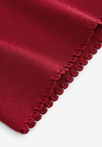 Tissu en coton bourgogne avec une surface texturée, présentant un bord festonné. Le tissage est lisse avec une légère brillance.