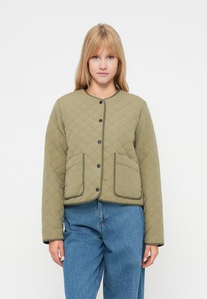 Olivgrüne gesteppte Jacke mit rundem Ausschnitt, Druckknopfverschlüssen, zwei vorderen Taschen und schwarzen Besatzdetails. Gestylt mit blauen Denim-Jeans.