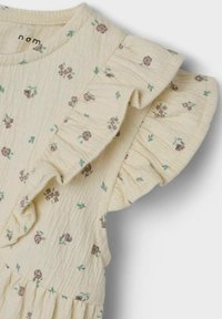 Robe florale jaune avec des manches volantes, ornée de petites fleurs bordeaux et de feuilles vertes, fabriquée en tissu texturé avec une finition douce.