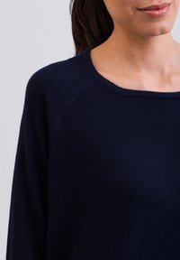 Pull bleu marine avec un col large et de longues manches raglan, fabriqué dans un tissu doux et texturé. Pas de motifs ni de quincaillerie visibles.