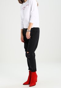 Felpa bianca con logo "Calvin Klein", jeans neri scoloriti e stivaletti alla caviglia rossi in suede con tacco blocco. Modella in piedi.