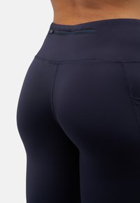 Högmidjade marinblå leggings i elastisk tyg, med en liten dragkedjeficka bak och flatlock-sömmar för komfort.