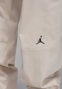 Beige bomullbyxor med en svart broderad Jumpman-logotyp, med en avslappnad passform och sydda detaljer längs sidoseam.