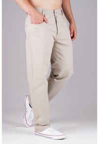 Beige Baumwollhosen mit geradem Schnitt, vorderen Taschen und Reißverschluss. Kombiniert mit weißen Sneakers mit roten und blauen Akzenten.
