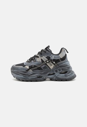 Zwarte en grijze sportschoenen met een bovenwerk van mesh en synthetisch materiaal, prominente golvende zool, reflecterende accenten en een gelaagd ontwerp.
