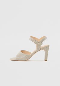 Åpen-tå heeled sandal i lys gull teksturert materiale. Har en tynn ankelstropp med spenne og en avsmalnende hæl. Flat såle.