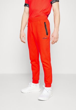 Rode sweatpants met een taps toelopend ontwerp, elastische tailleband en een zwarte ritszak. Combinatie met witte sportschoenen.