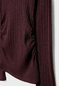 Weinroter, gerippter Stoff mit vertikaler Textur, der an einer Seite weich fällt und an den Rändern eine glatte Oberfläche aufweist.