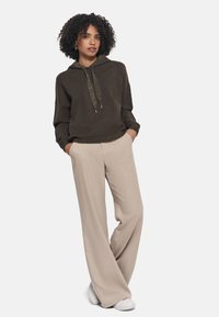 Sudadera corta de color verde oscuro con cordón y acentos metálicos, combinada con pantalones de pierna ancha de color beige claro y zapatillas blancas.