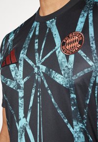 Musta urheilupaita, jossa sinisiä geometrisia kuvioita, punainen Adidas-logo ja FC Bayern Münchenin tunnus. Sileä kangaspinta.