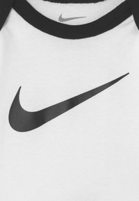 T-shirt en coton blanc arborant un logo Nike swoosh noir bien en vue, bordé d'un col en ribbed noir et de finitions noires sur les épaules.