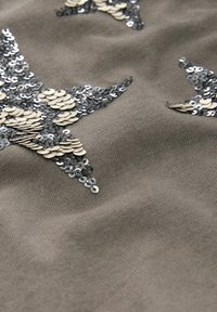 Tissu gris avec trois formes d'étoiles en sequins argentés et crème, présentant une texture douce et un léger éclat.