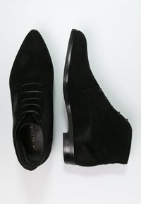 Bottines en daim noir à bouts pointus, présentant une texture lisse, un design à lacets et une semelle plate élégante. Détails minimaux sur le côté.