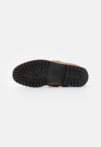 Sula på kängor med djupt svart mönster och Timberland-logga, sedd från botten på en vit bakgrund.