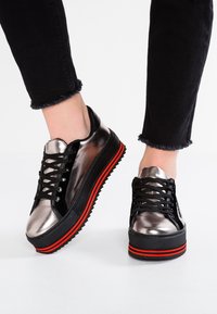 Baskets plateformes métalliques argentées avec des lacets noirs, une semelle noire et des accents rouges. Présente une finition texturée et un design volumineux.