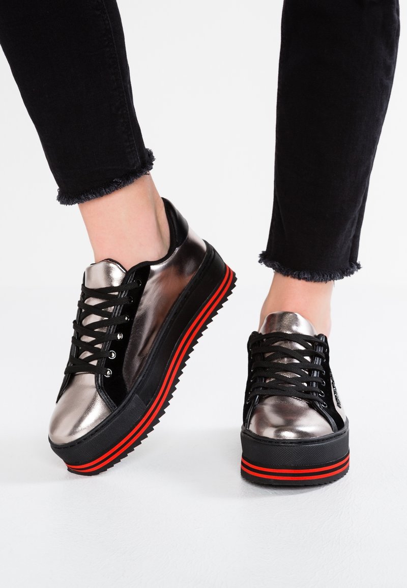 Baskets plateformes métalliques argentées avec des lacets noirs, une semelle noire et des accents rouges. Présente une finition texturée et un design volumineux.