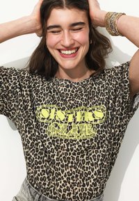 T-shirt à imprimé léopard en beige et noir avec un graphique néon jaune "Sister Club". Manches courtes et coupe décontractée. Texture de tissu lisse.