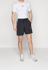 Adidas träningskläder bestående av en figursydd vit t-shirt med kort ärm och svarta shorts med vita sidostreifen, elastisk midja och logodetaljer.