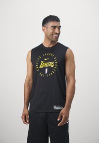 Camiseta preta sem mangas da Nike com texto amarelo "Lakers" e um logótipo da NBA. Tecido macio com um corte descontraído, combinada com calções de atletismo pretos.