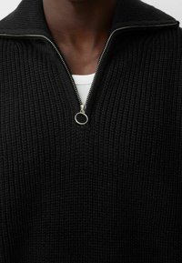 Svart stickad tröja med halvlång dragkedja, med texturerad yta och ståkrage. Silverfärgad dragkedja synlig.