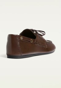 Scarpa in pelle marrone con suola piatta, caratterizzata da lacci e dettagli di cucitura, punta tonda e occhielli in metallo sui lati.