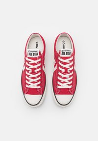 Rote Leinensneaker mit weißen Schnürsenkeln, Gummikappe am Zehenbereich und kontrastierendem weißen Stern-Logo. Schwarze Umrandung um die Sohle.