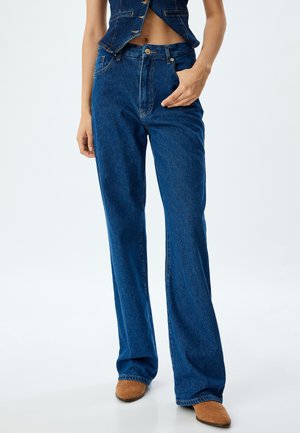 Jean flare en denim bleu avec taille haute, coutures contrastées et fermeture à bouton sur le devant. Texture lisse et design à jambe large.