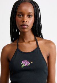 Top halter nero con un design aderente, impreziosito da ricami di rose rosa e stelle dorate. Realizzato in tessuto liscio con una finitura opaca.