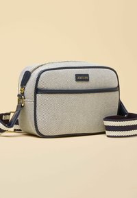 Sac bandoulière beige et marine avec motif texturé, fermeture éclair dorée, poche avant, et sangle d'épaule réglable rayée, étiquette de marque "Joules".