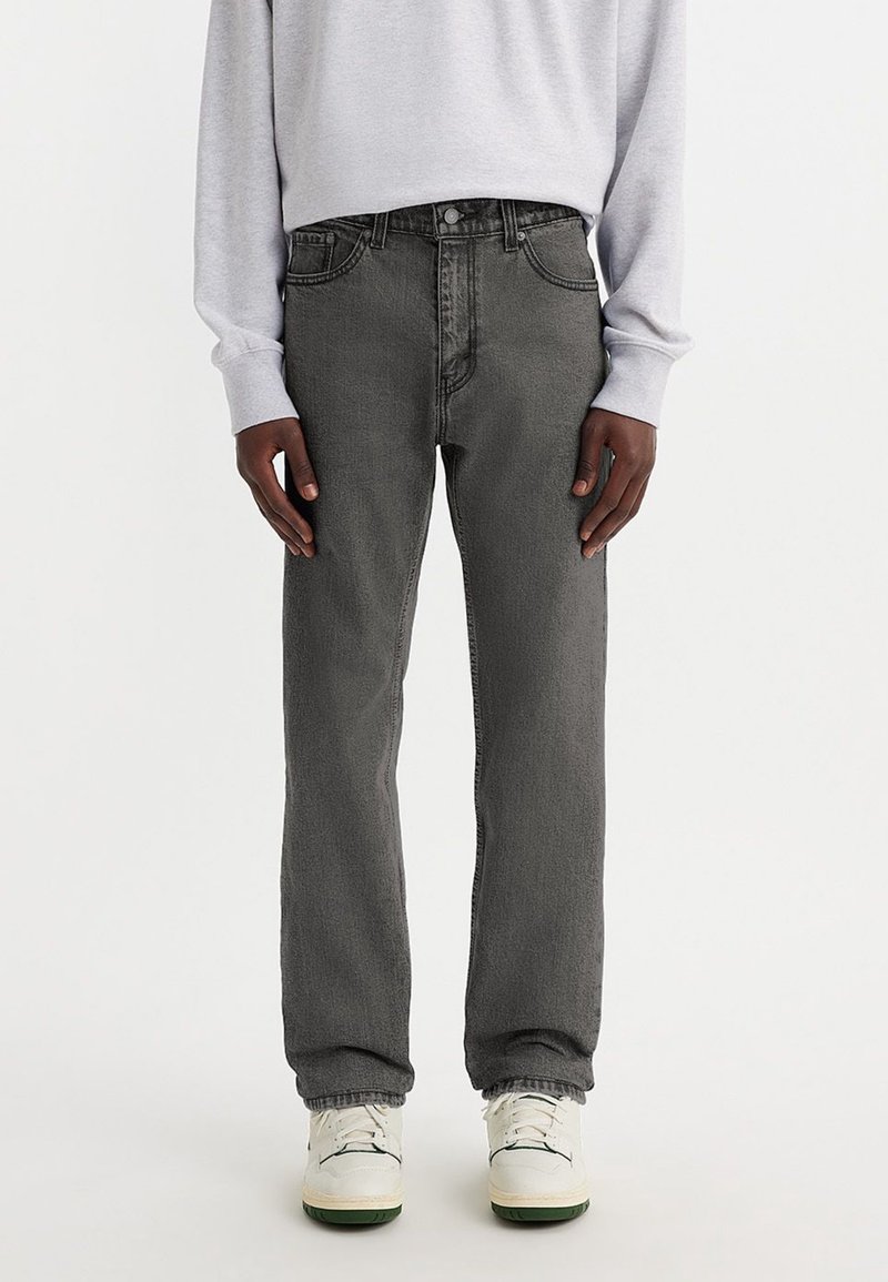 Jeans de mezclilla gris con un diseño de pierna recta, cinco bolsillos y cierre de botones. Llevados con un sudadera gris claro y zapatillas blancas.