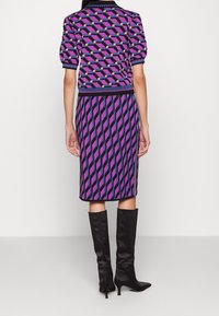 Completo lavorato a maglia in viola e nero con motivi geometrici; presenta maniche corte, polsini a coste e una gonna aderente. Abbinato a stivali neri al ginocchio.