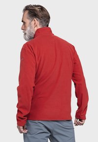 Rote Fleecejacke mit hohem Kragen und langen Ärmeln, die eine glatte Textur aufweist. Die Rückansicht zeigt ein schlichtes Design ohne sichtbare Markierungen.