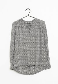 Blouse à manches longues sur un cintre, en tissu léger, avec un motif géométrique noir et blanc, un col en V et des manches froncées.