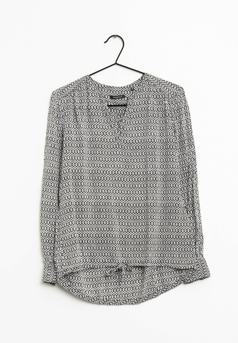 Blouse à manches longues sur un cintre, en tissu léger, avec un motif géométrique noir et blanc, un col en V et des manches froncées.